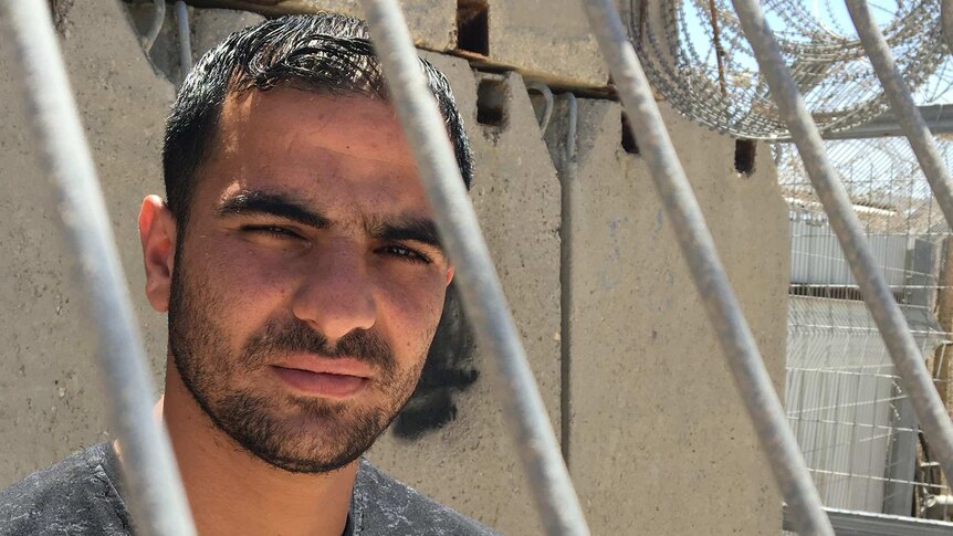 A man, Anan, stands behind a fence after visiting his sister at Ofer military prison.