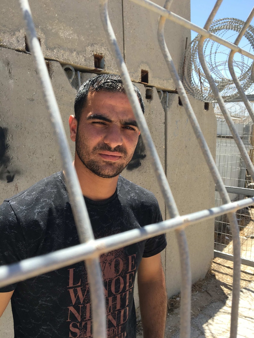 A man, Anan, stands behind a fence after visiting his sister at Ofer military prison.