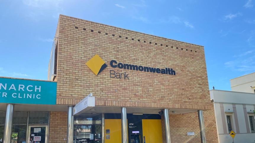 A cream brick building with Commonwealth Bank sign and yellow windows and ATM on a country street.