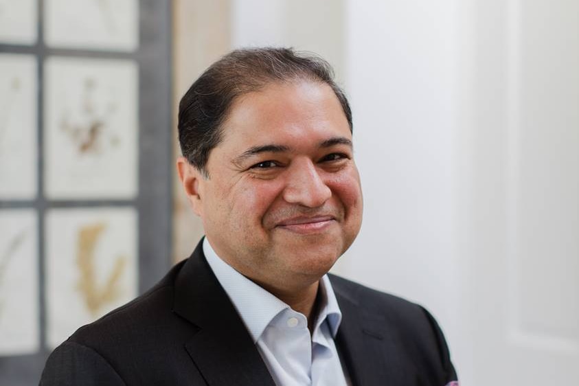 Sydney plastic surgeon Dr Naveen Somia smiles as he poses for a photo. He is wearing a suit and tie. 