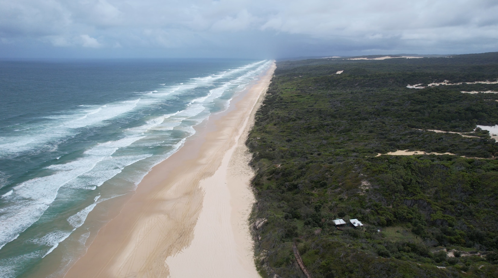 Una vista aérea del océano, la playa de arena blanca y el bosque verde.