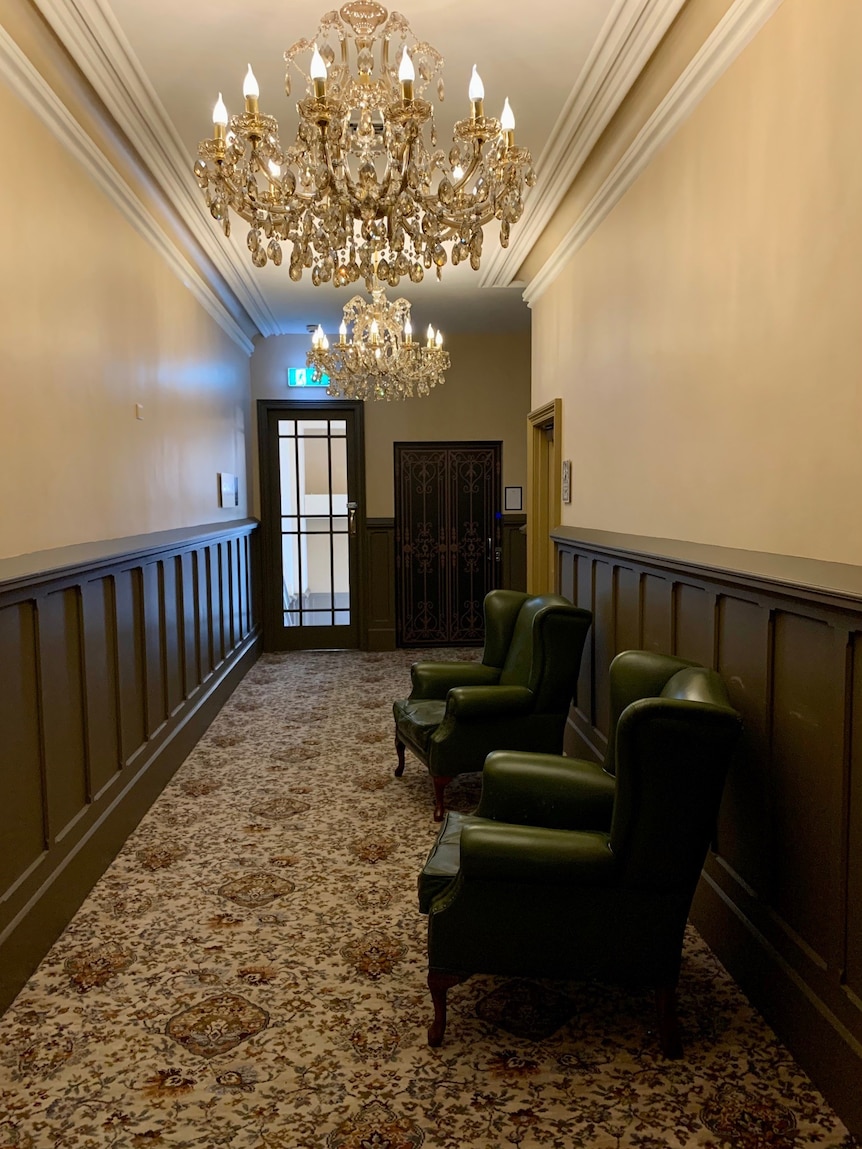 in a hallway a chandelier hangs from the ceiling, underneath are two leather armchairs
