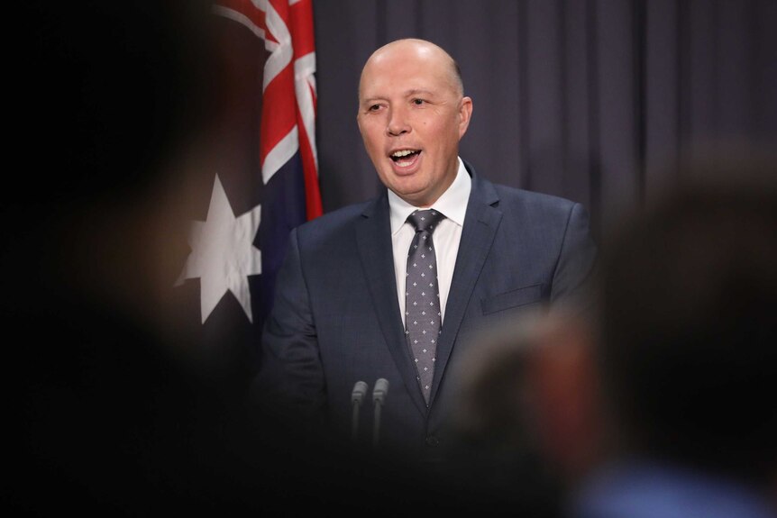 Dutton seen through a blurry foreground, smiling at a lectern.