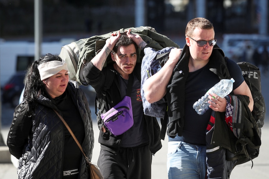 three people carry bags and suitcases across the russian border 