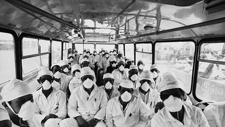 A group of scientists in white coats, hats and masks sit crowded in a bus