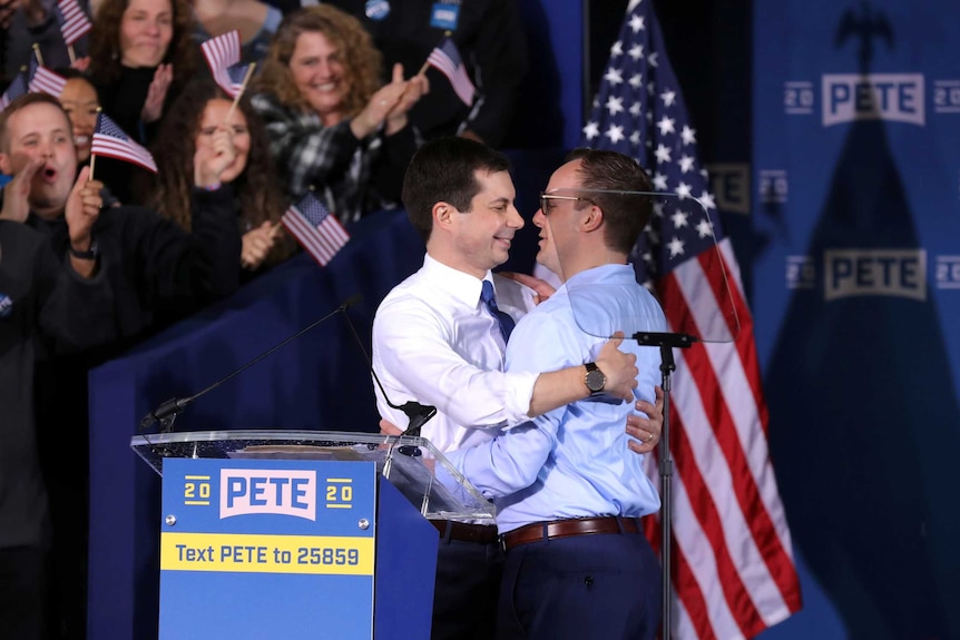 Pete Buttigieg embraces his husband Chasten while supporters cheer and wave American flags