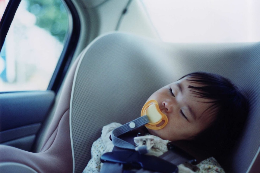 A young girl with a dummy in her mouth asleep in the back of a car