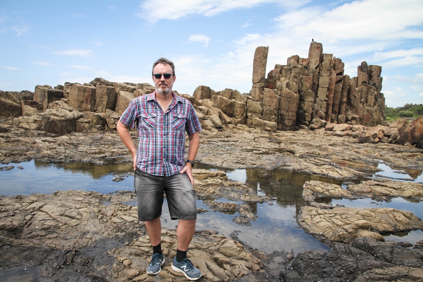 Soloman Buckland stands in front of a coastal rock formation.