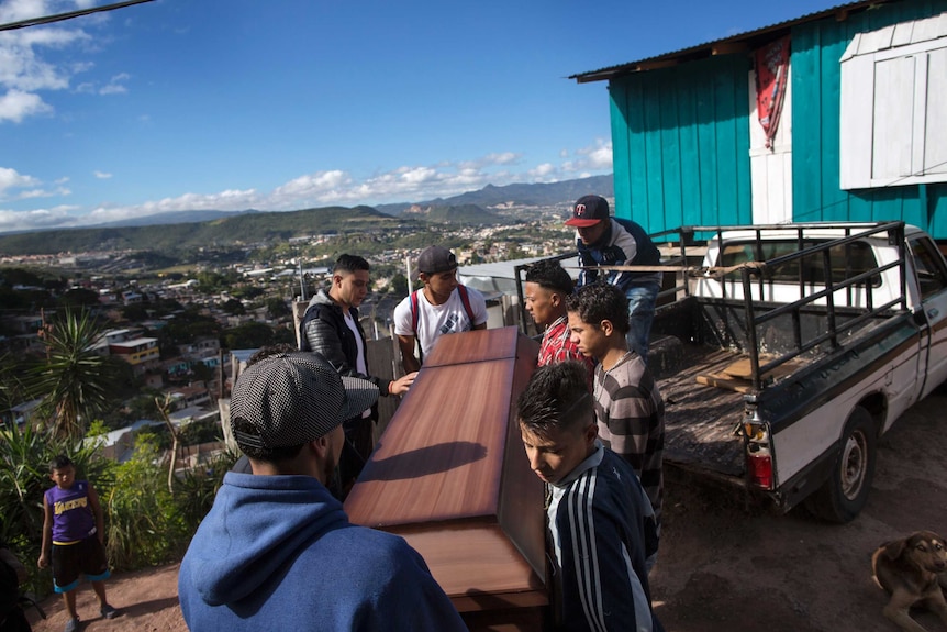 A group of men lift a coffin off the back of a truck.