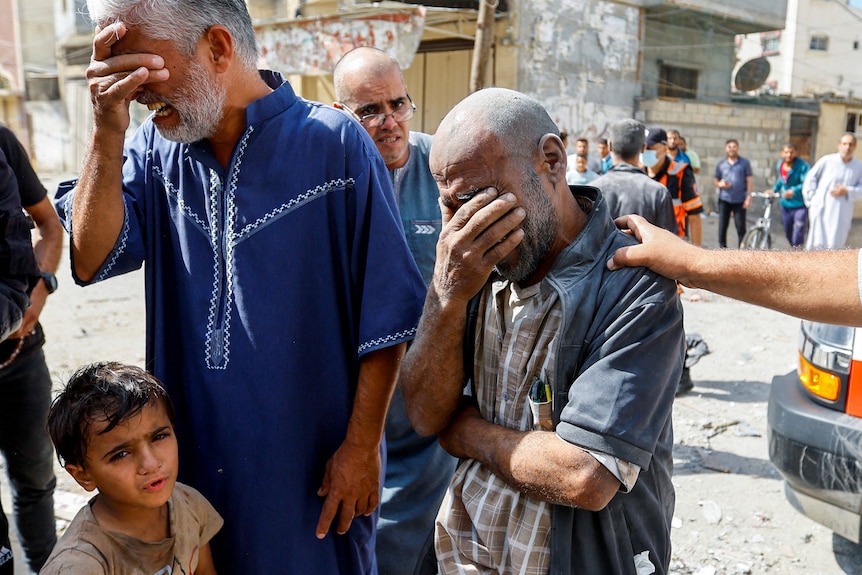 Two men stand with their heads in their hands. A young boy stands in front of them. 