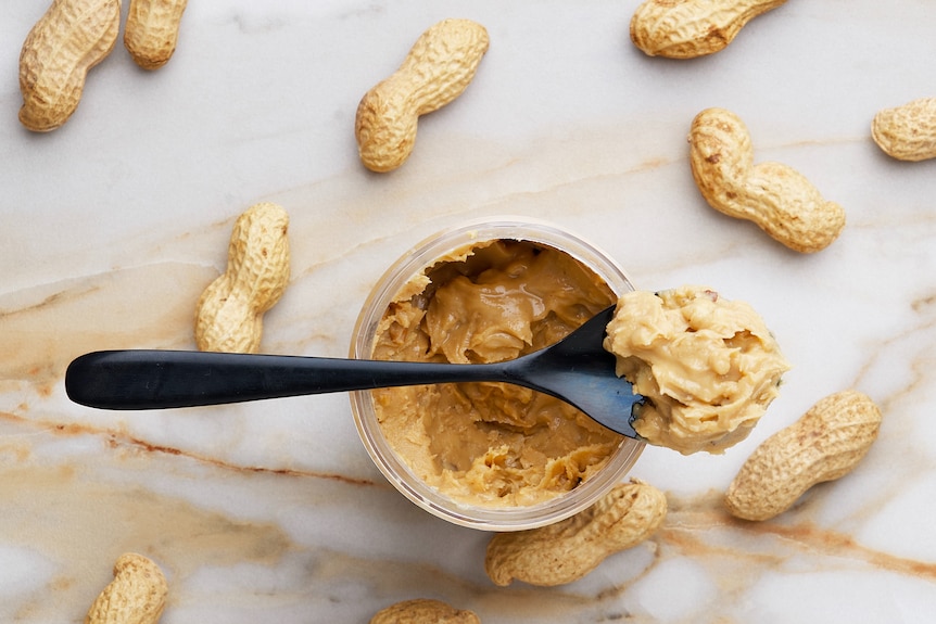 A spoonful of peanut butter with peanuts in background