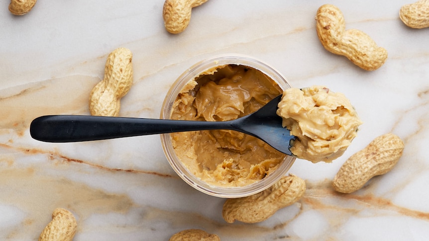 A spoonful of peanut butter with peanuts in background.