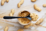 A spoonful of peanut butter with peanuts in background