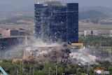 A large black multi-storey building is pictured as it is being demolished.