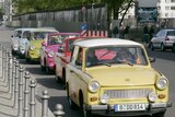 Trabant cars drive in front of the remains of the 'Mauer' frontier wall