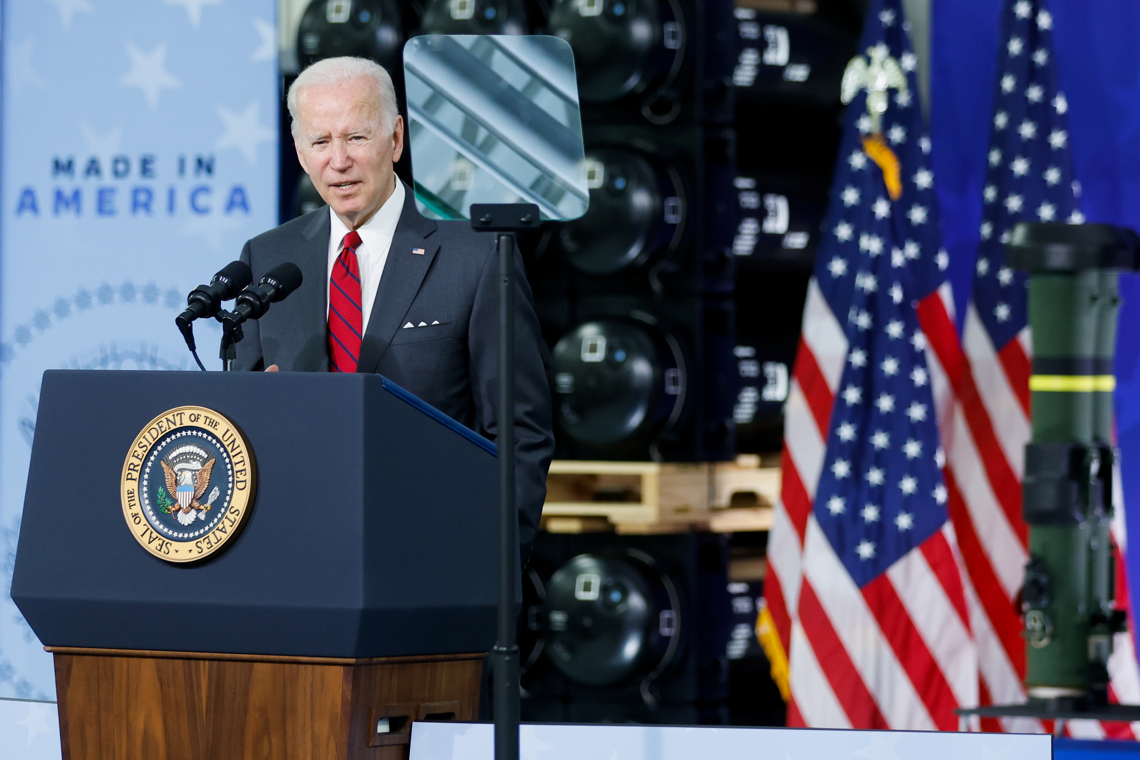 乔·拜登站在一家武器工厂的讲台前，面前是一个写着“美国制造”的标志。 
