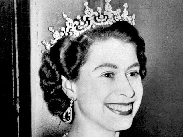 A black and white photo of the Queen in a tiara grinning 