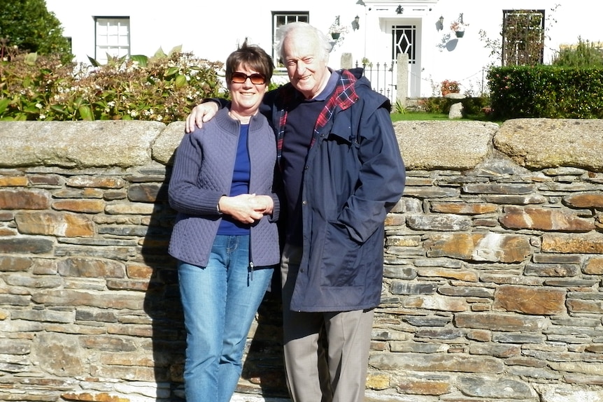 A photo of a woman and man standing, in front of brick wall 