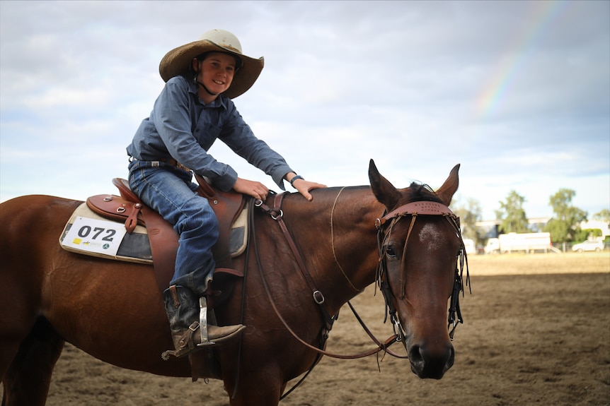 A young boy on a numbered horse in an outback setting