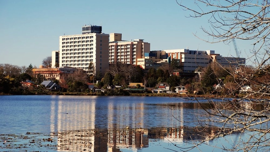 A large white and brown brick hospital building overlooks a lake in Waikato, New Zealand.