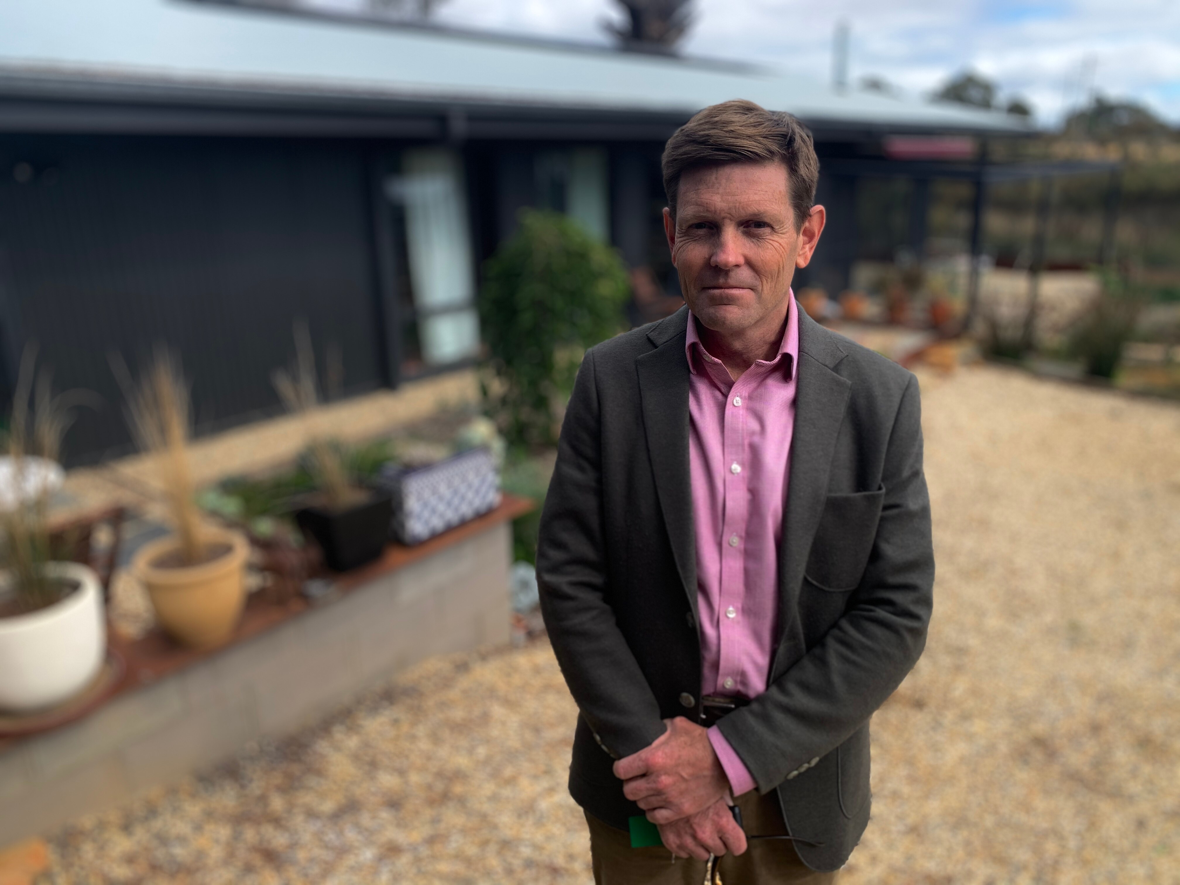 A man wearing a pink shirt and grey jacket.
