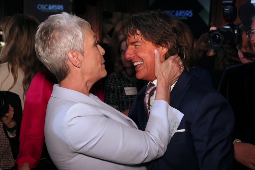 Jamie Lee Curtis holds Tom Cruise's face in a crowded room. 