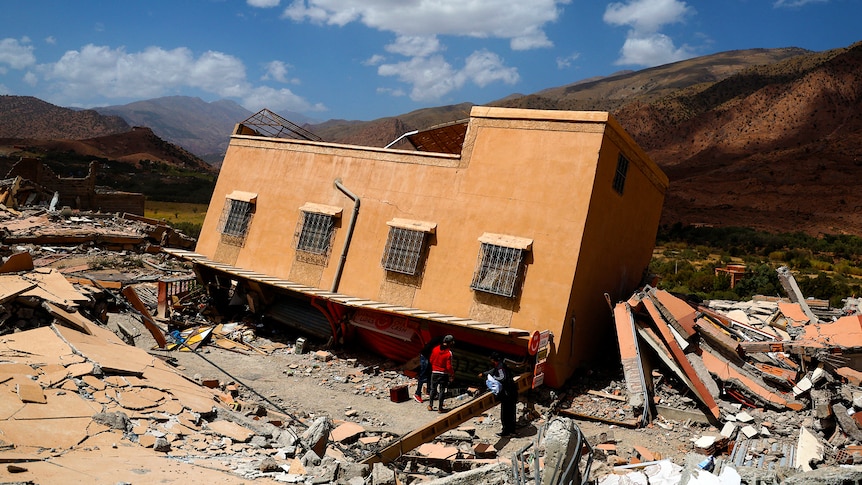 People stand amidst rubble near a damaged building in Talat N'Yaaqoub, Morocco.