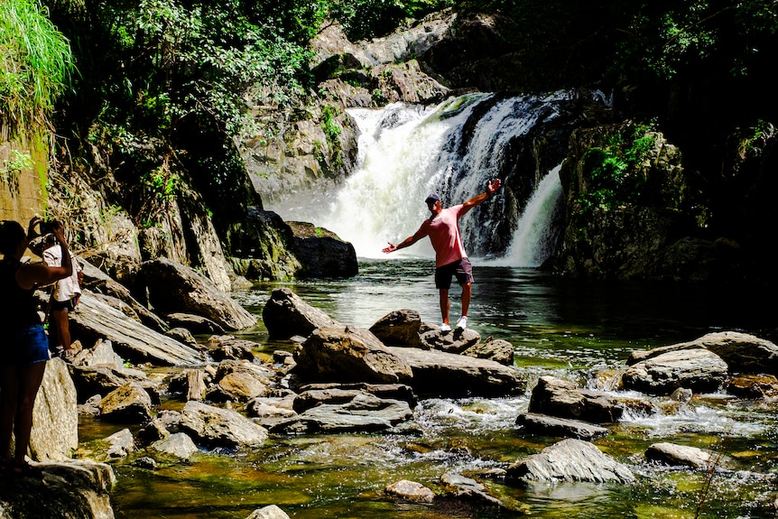 Man posing for photo in front of tropical rainforest waterfall.
