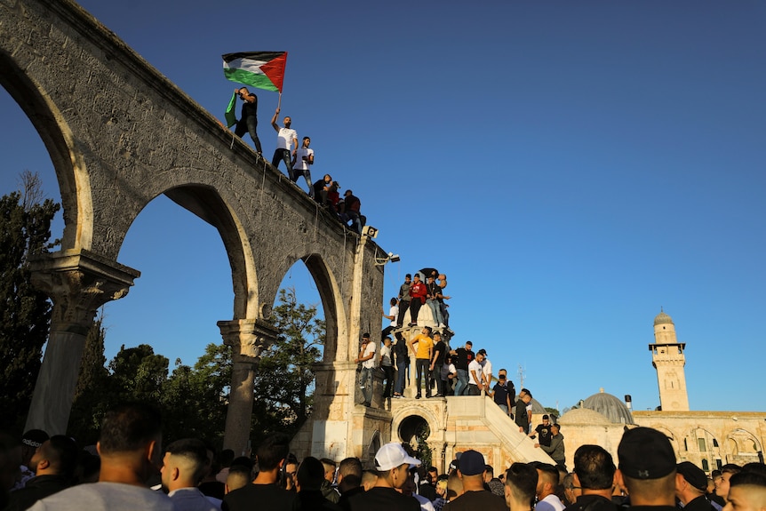 People wave Palestinian flags while standing on a stone arch at al-Aqsa mosque compound