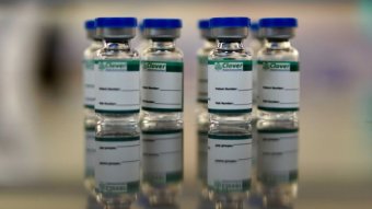 Small glass bottles containing the vaccine are on a metal tray.