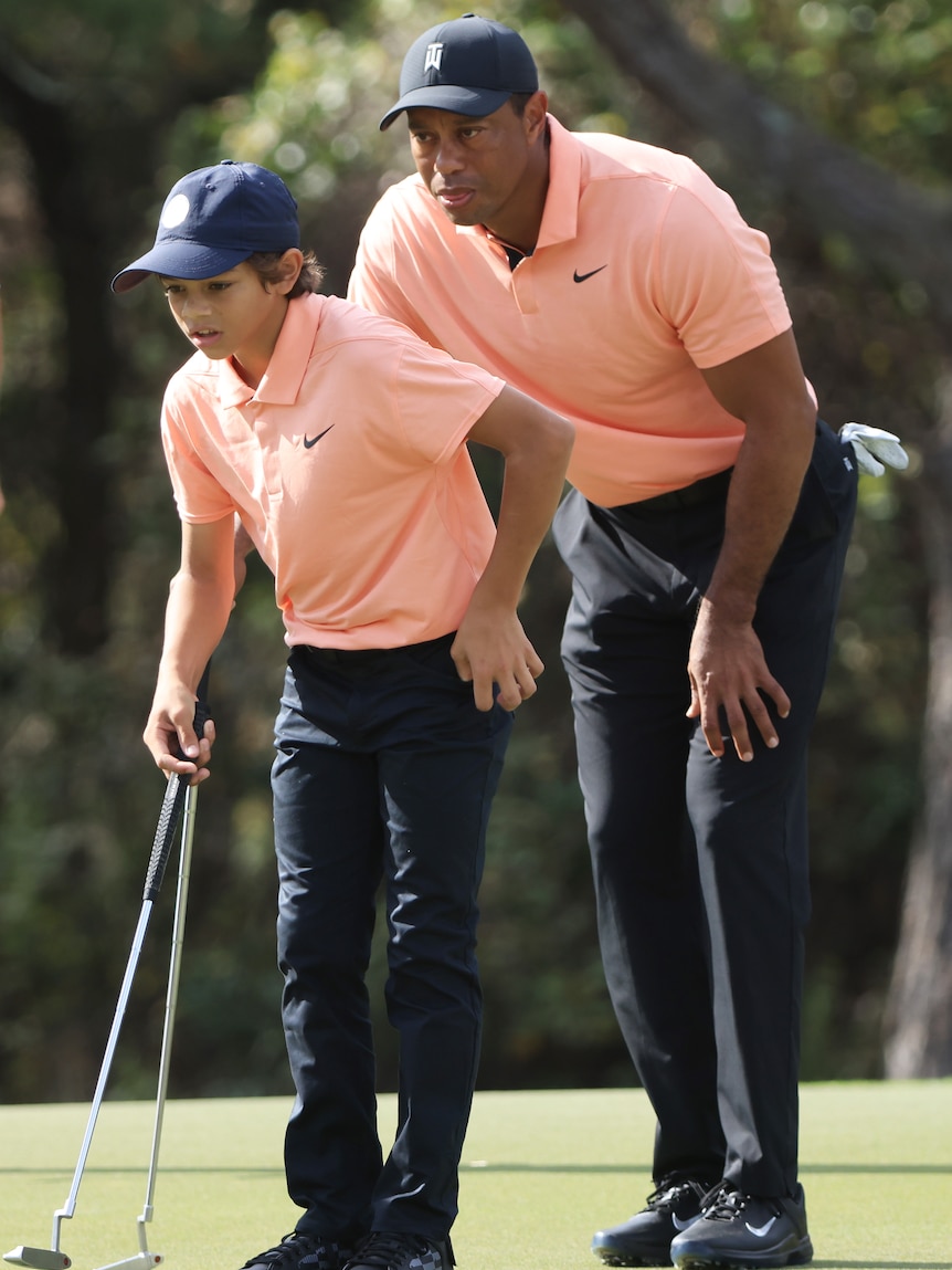 A son and his father look at a ball on a golf green