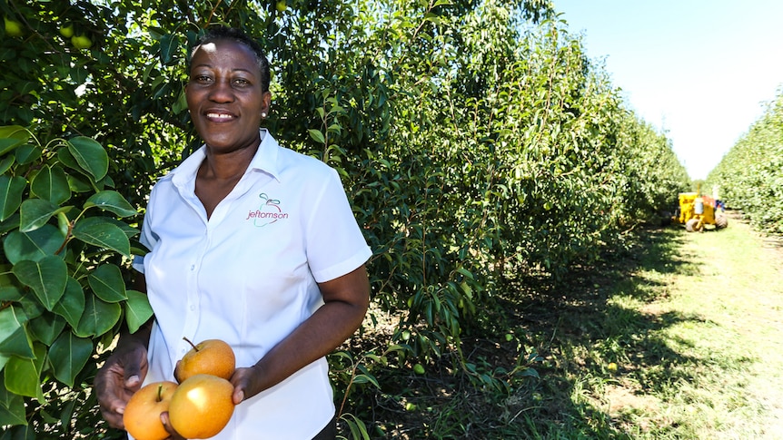 Olabisi Oladele  standing beside a row of fruit trees.