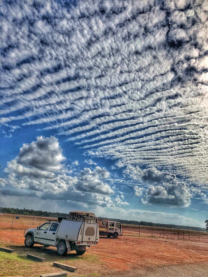 ABC car parked on red dirt with stunning clouds in rows.