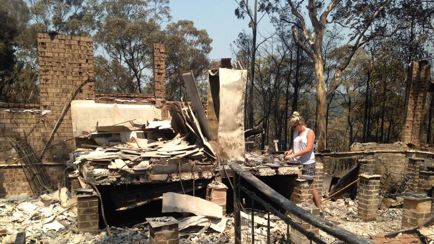 A woman inspects the ruins of her fire damaged house