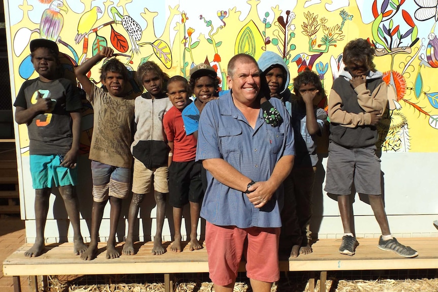 Tjuntjuntjara RCS Principal Charlie Klein with some of his students in front of a mural.