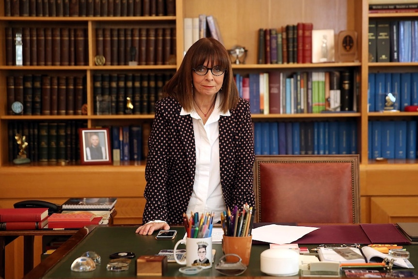 Katerina Sakellaropoulou standing up on a desk in an office filled with books.
