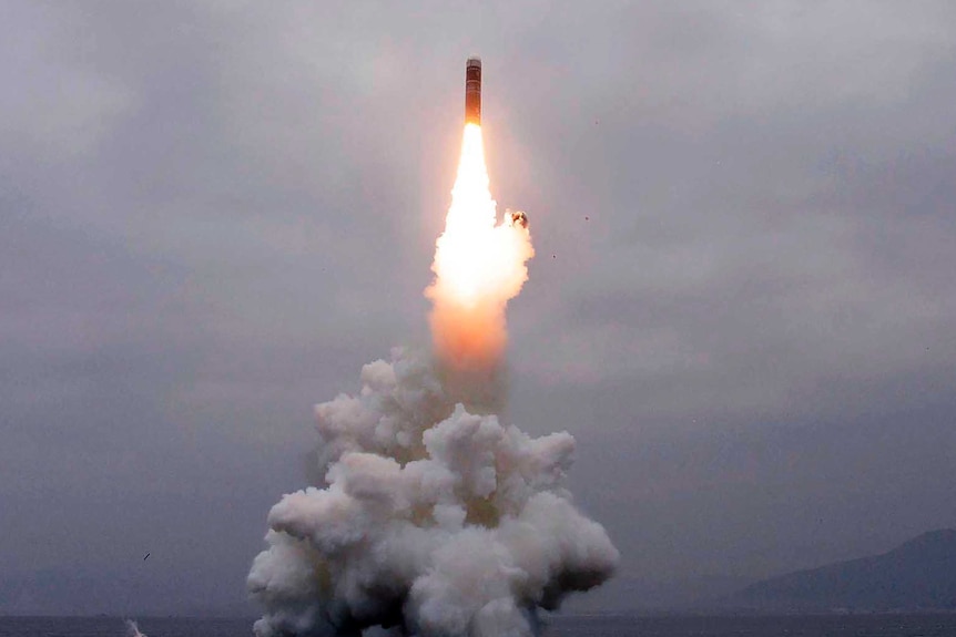 A missile launches from the sea, leaving behind a trail of smoke.