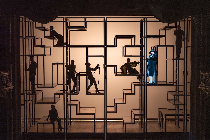Performers in silhouette move among a complex stage set that looks like a backlit vertical maze.