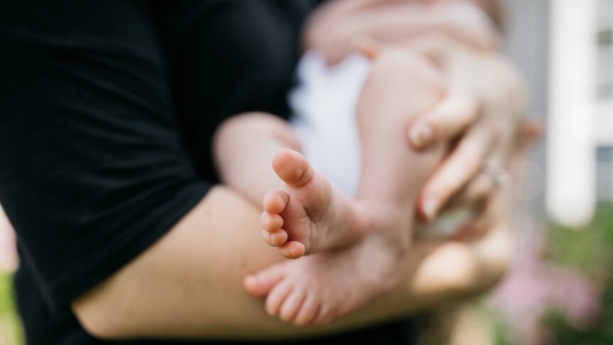 Blurred photo of parent holding a baby, with the baby's feet in focus.
