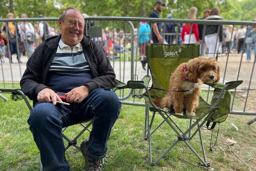 A middle-aged man sits in a camping chair next to his dog in another chair.