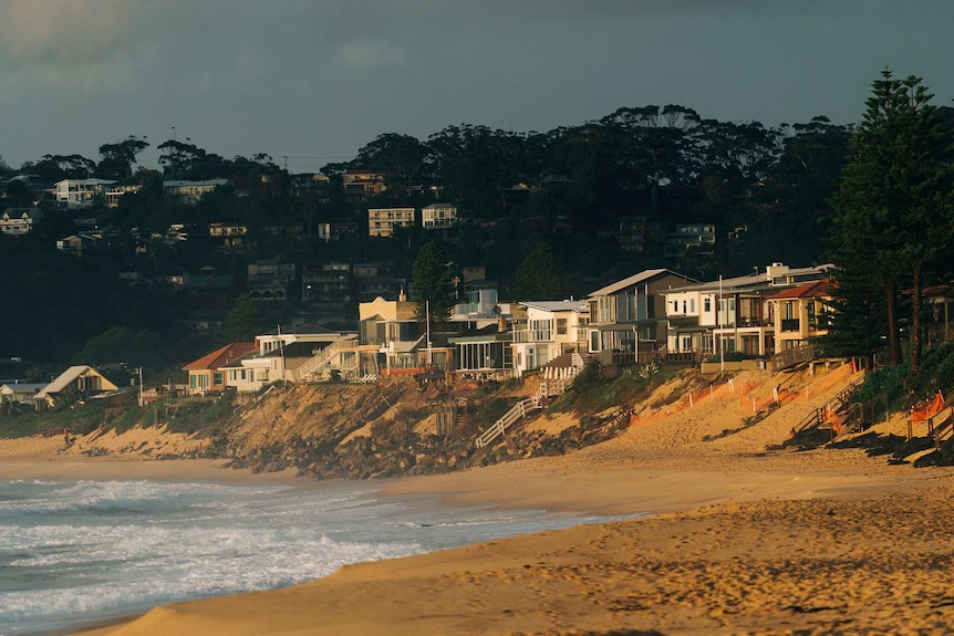 Telephoto lens shot of Wamberal Beach houses eroded with sunrise warm light glinting against the houses.
