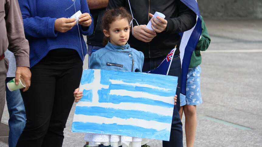 A young girl holding a handpainted flag of Greece
