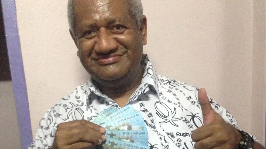 Man holds up banknotes in right hand and puts left thumb up.