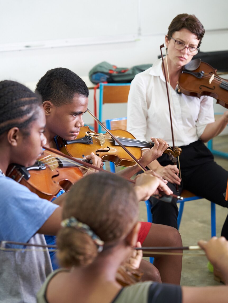 A woman teaching young kids strings.