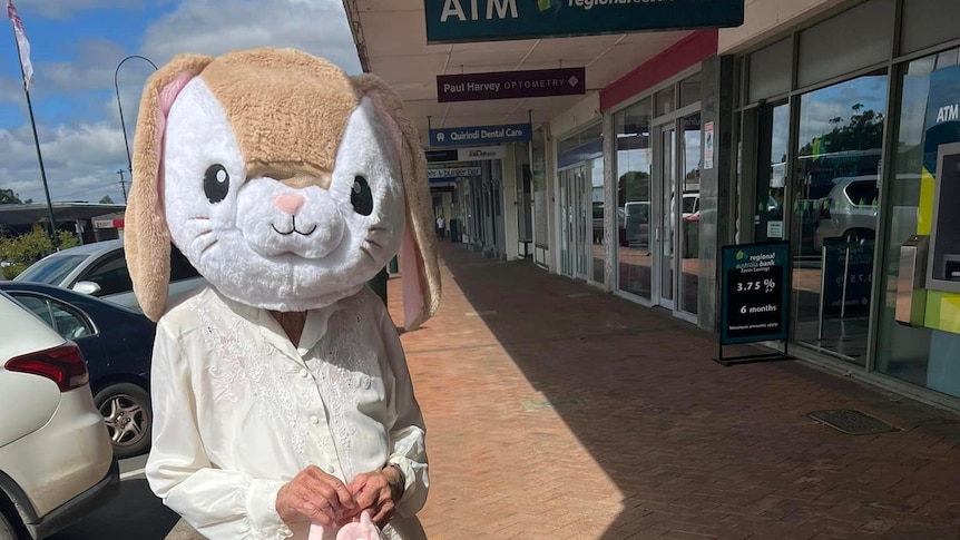 A picture of a person dressed as a rabbit, standing on a paved street footpath. 