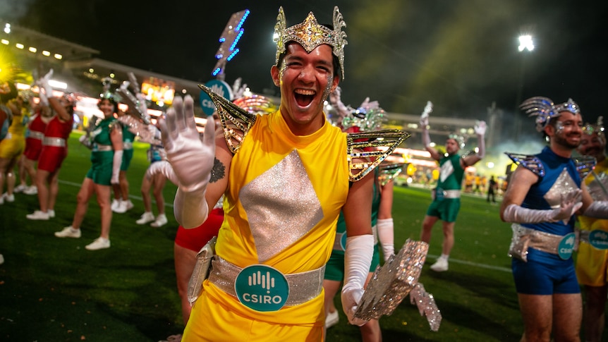 a  man smiling wearing a yellow outfit and silver headdress