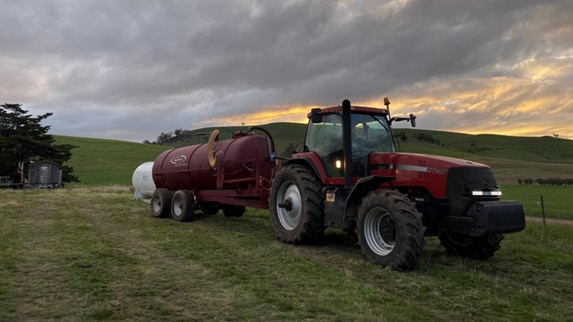 A tractor hauls a tank through a paddock.