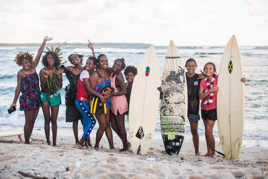 A group of nine women and girls from Vanuatu posing with surf boards on the beach.