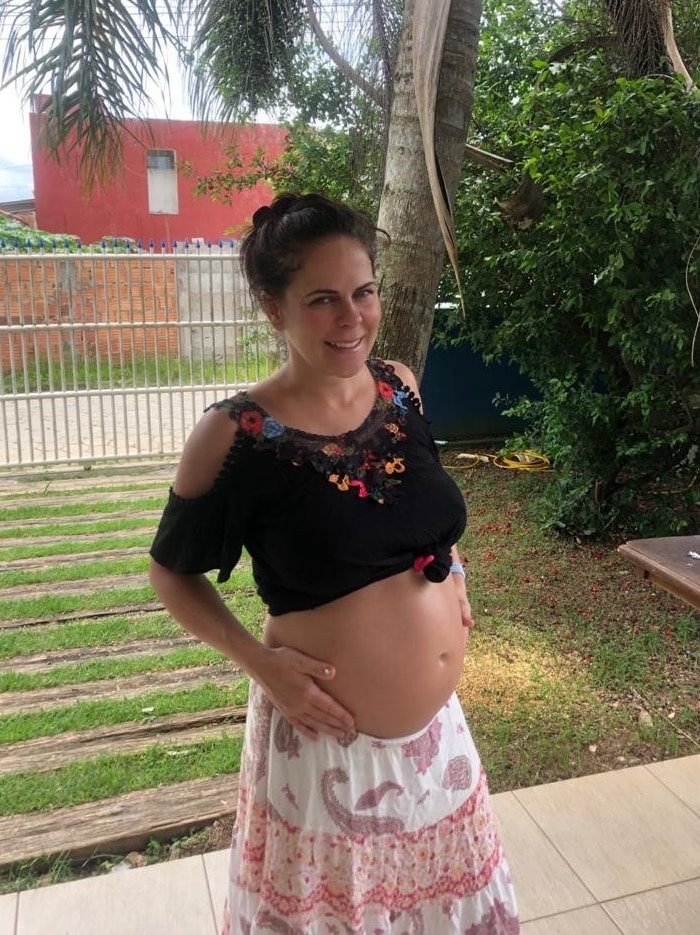 A woman stands holding her pregnant belly