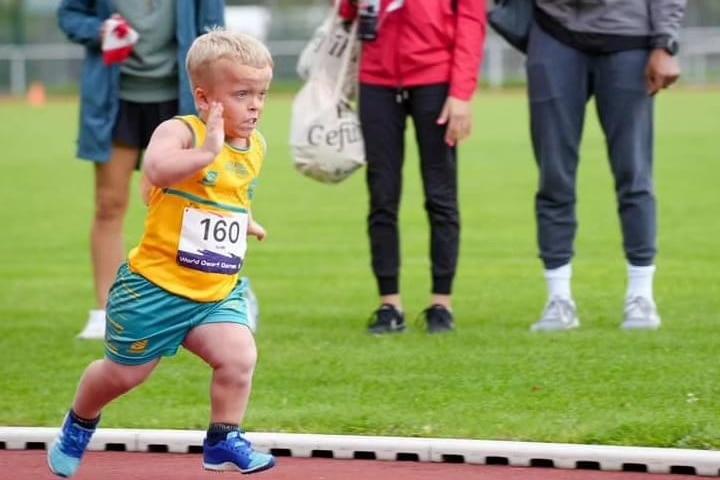 A young boy in an Australian sports uniform runs around a track.